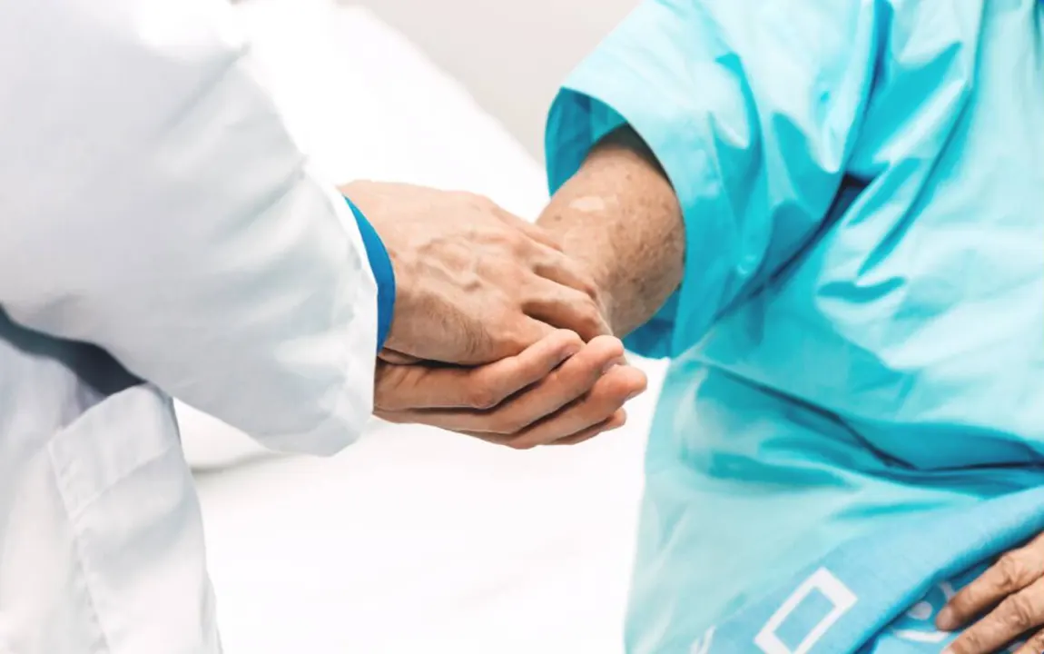 Médico tomando la mano de un paciente adulto como gesto de acompañamiento